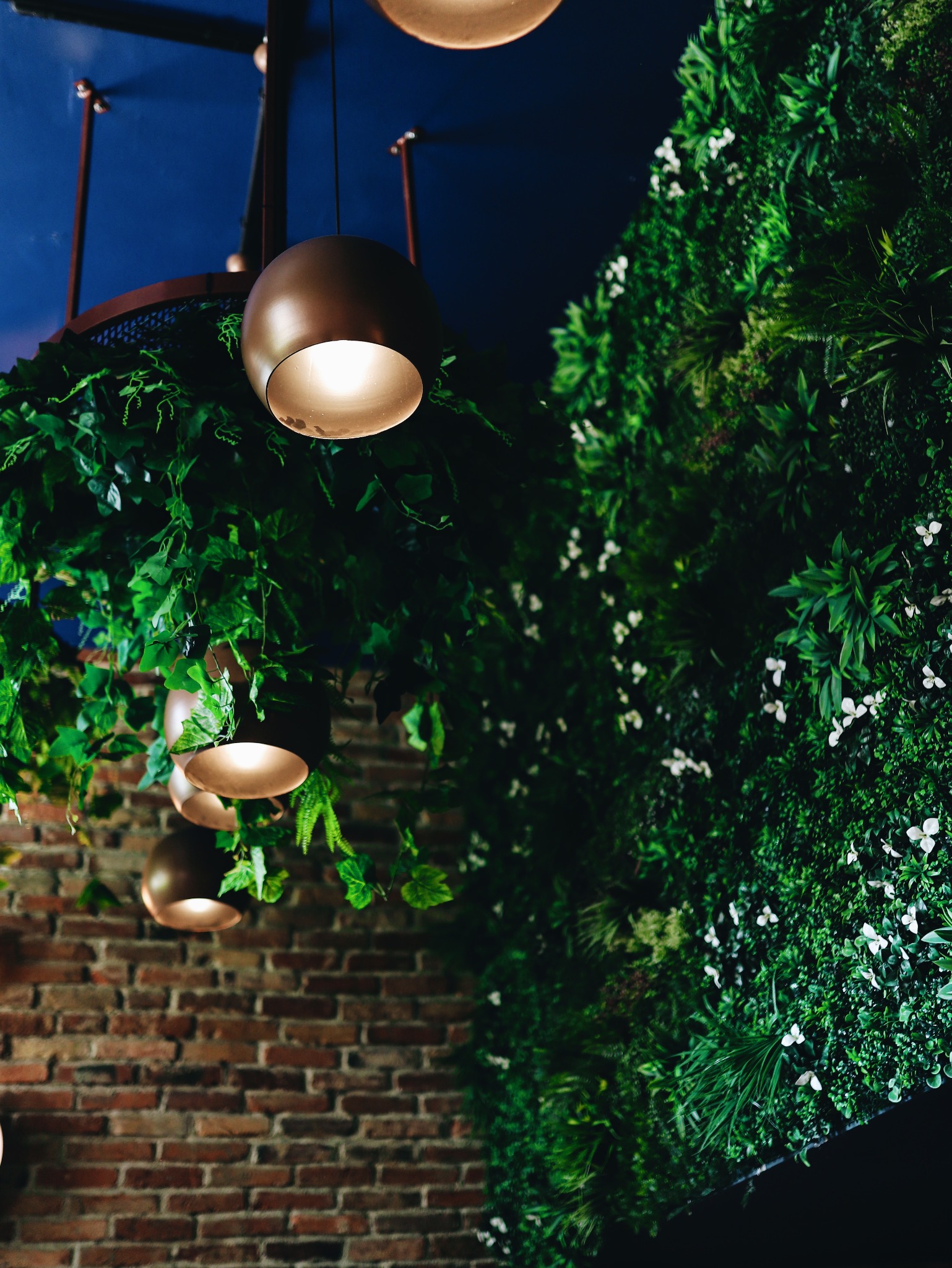 Dekoracja wnętrza restauracji: sztuczna ściana z roślin, wiszące lampy w kształcie kul i ściana z czerwonej cegły.