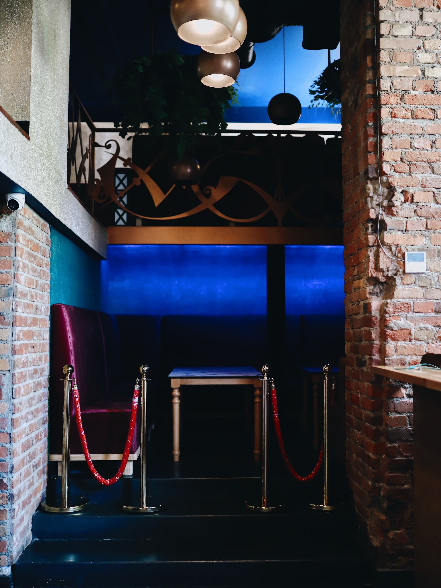 Wejście do klubu z czerwonymi sznurami odgradzającymi, ceglanymi ścianami i nastrojowym niebieskim oświetleniem w tle.