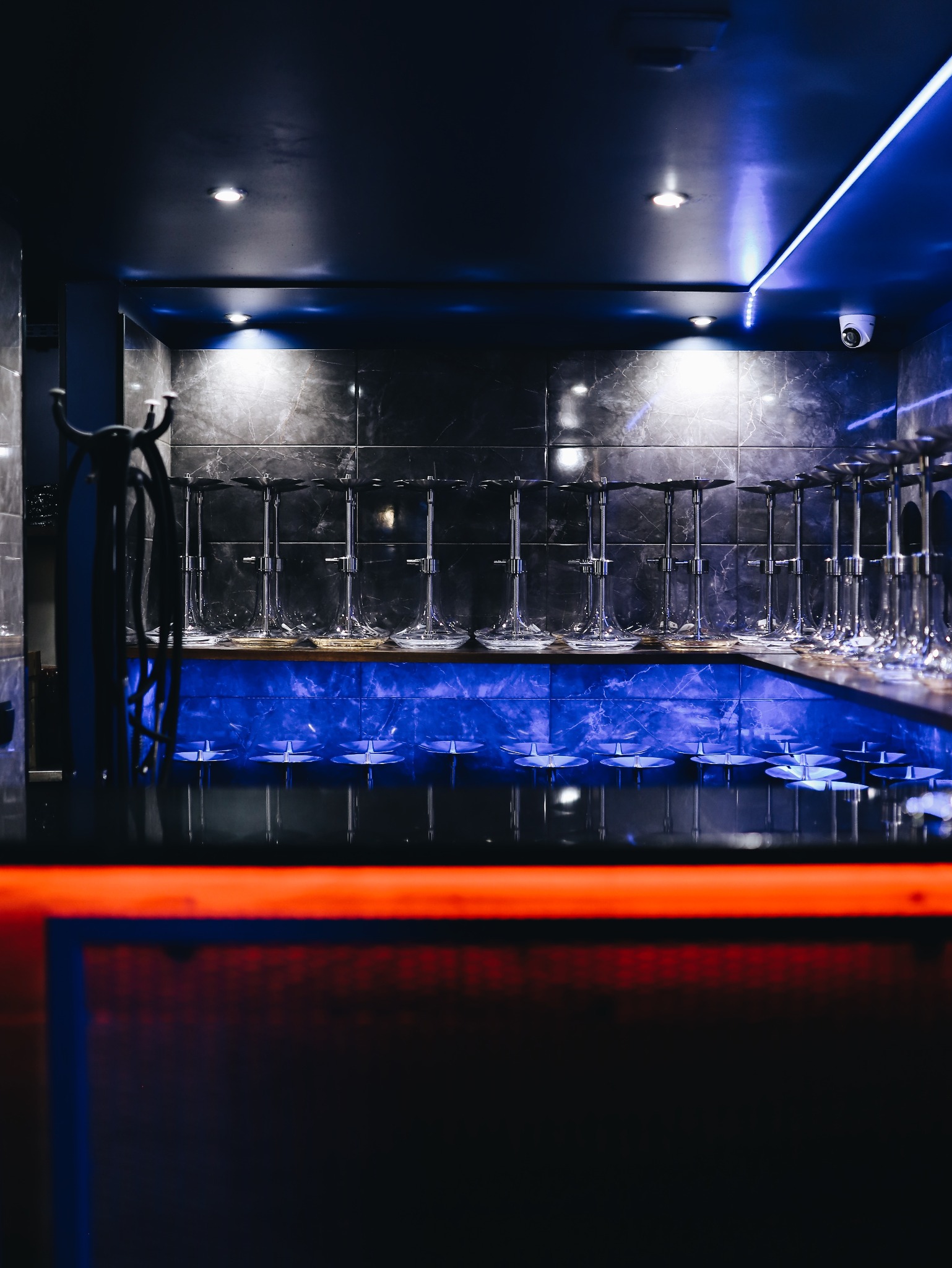 Rząd szklanych fajek wodnych ustawionych na podświetlonym blacie w ciemnym pomieszczeniu z marmurowymi płytkami i neonowym oświetleniem.