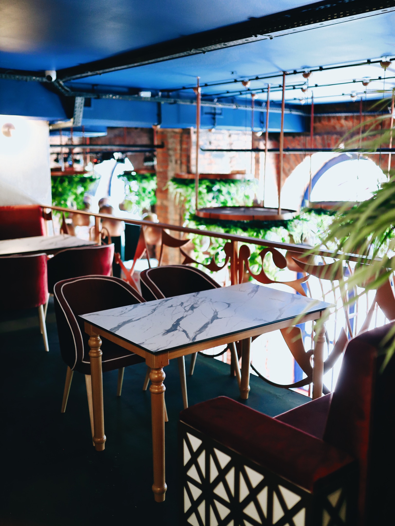 Eleganckie wnętrze restauracji z marmurowymi stolikami, czerwonymi krzesłami i dekoracyjną balustradą, widok z góry na niebieski sufit z oświetleniem.