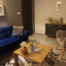 Pokój terapeutyczny z niebieską kanapą, drewnianym stolikiem kawowym z pudełkiem chusteczek i wodą, oraz wyciszonymi akustycznie drzwiami.