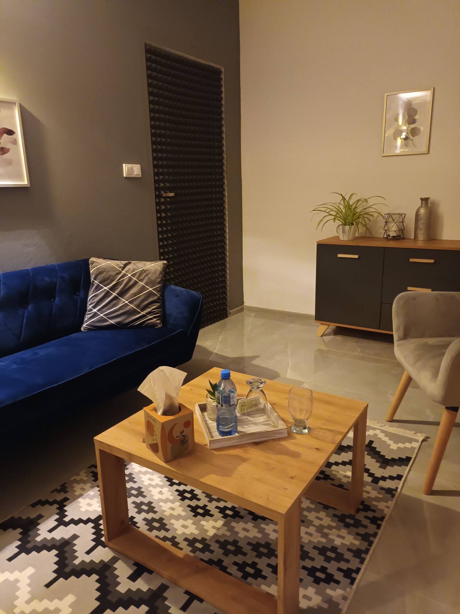 Pokój terapeutyczny z niebieską kanapą, drewnianym stolikiem kawowym z pudełkiem chusteczek i wodą, oraz wyciszonymi akustycznie drzwiami.