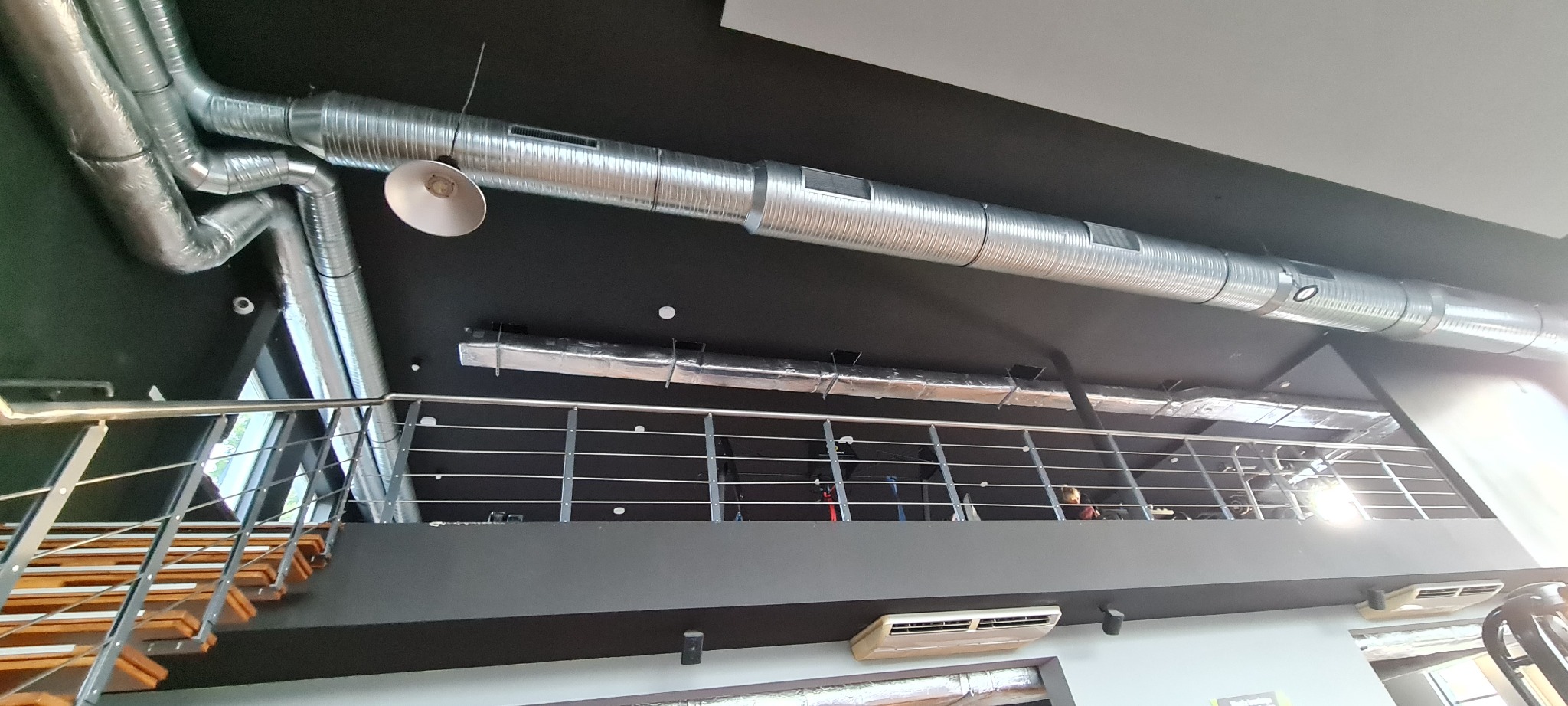 System wentylacyjny z rurami spiralnymi i klimatyzator kasetonowy w biurze w Warszawie, widoczne z perspektywy schodów.