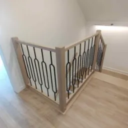 Drewniana balustrada schodowa z czarnymi, metalowymi prętami na jasnych schodach. Nowoczesny design, widok z góry.