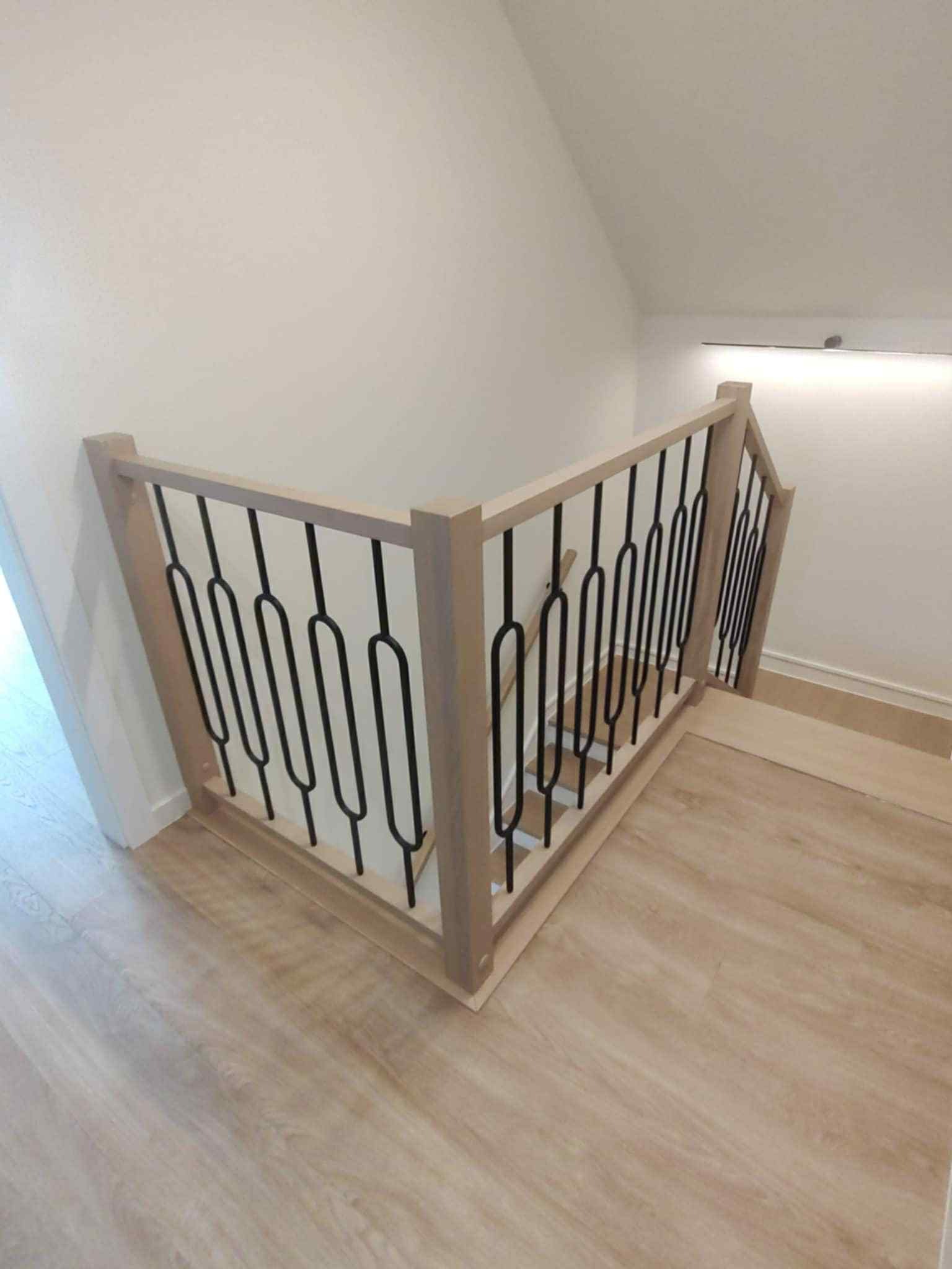 Drewniana balustrada schodowa z czarnymi, metalowymi prętami na jasnych schodach. Nowoczesny design, widok z góry.
