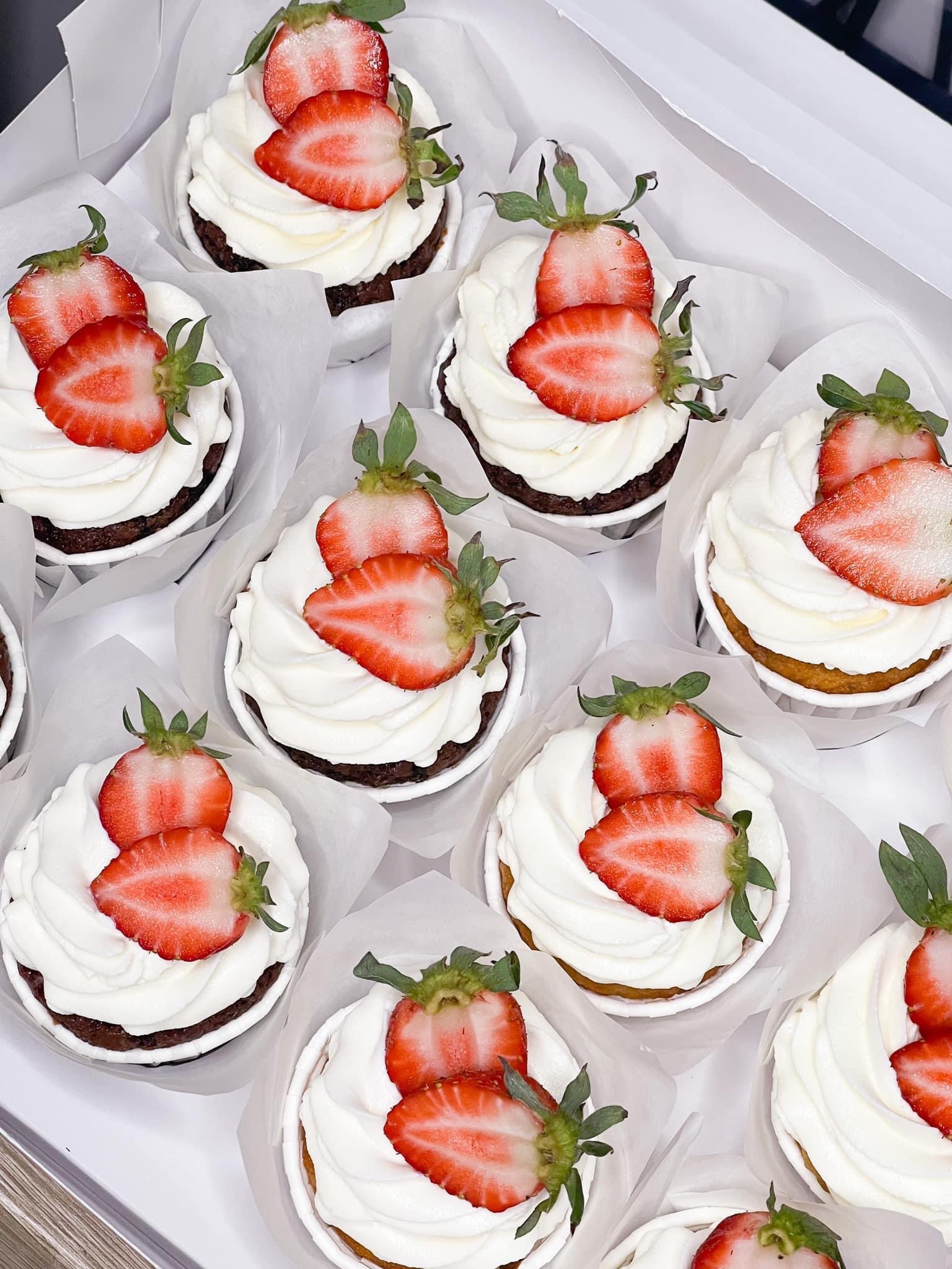 Karton z dziewięcioma babeczkami: czekoladowe i waniliowe spody, obfita warstwa białego kremu i dekoracja z dwóch plasterków świeżych truskawek z zielonymi szypułkami.