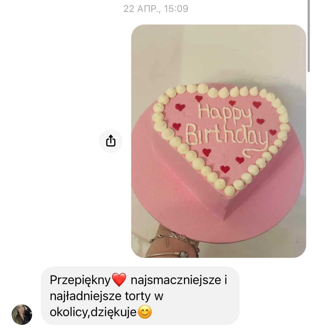 Różowy tort w kształcie serca z napisem 'Happy Birthday' i dekoracjami z białej kremówki oraz czerwonych serduszek, trzymany w dłoni z bransoletką, widok z góry w komunikatorze.