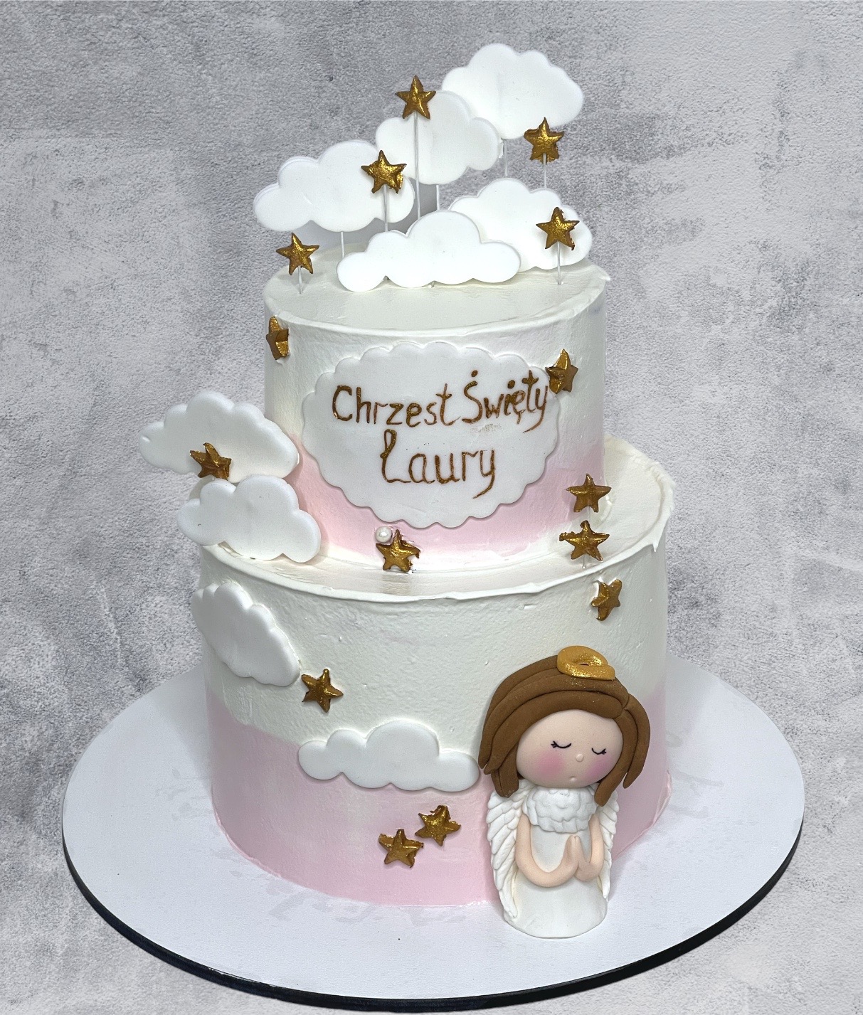 Dwupiętrowy tort na Chrzest Święty Laury, zdobiony białymi chmurkami, złotymi gwiazdkami i figurką aniołka z brązowymi włosami.