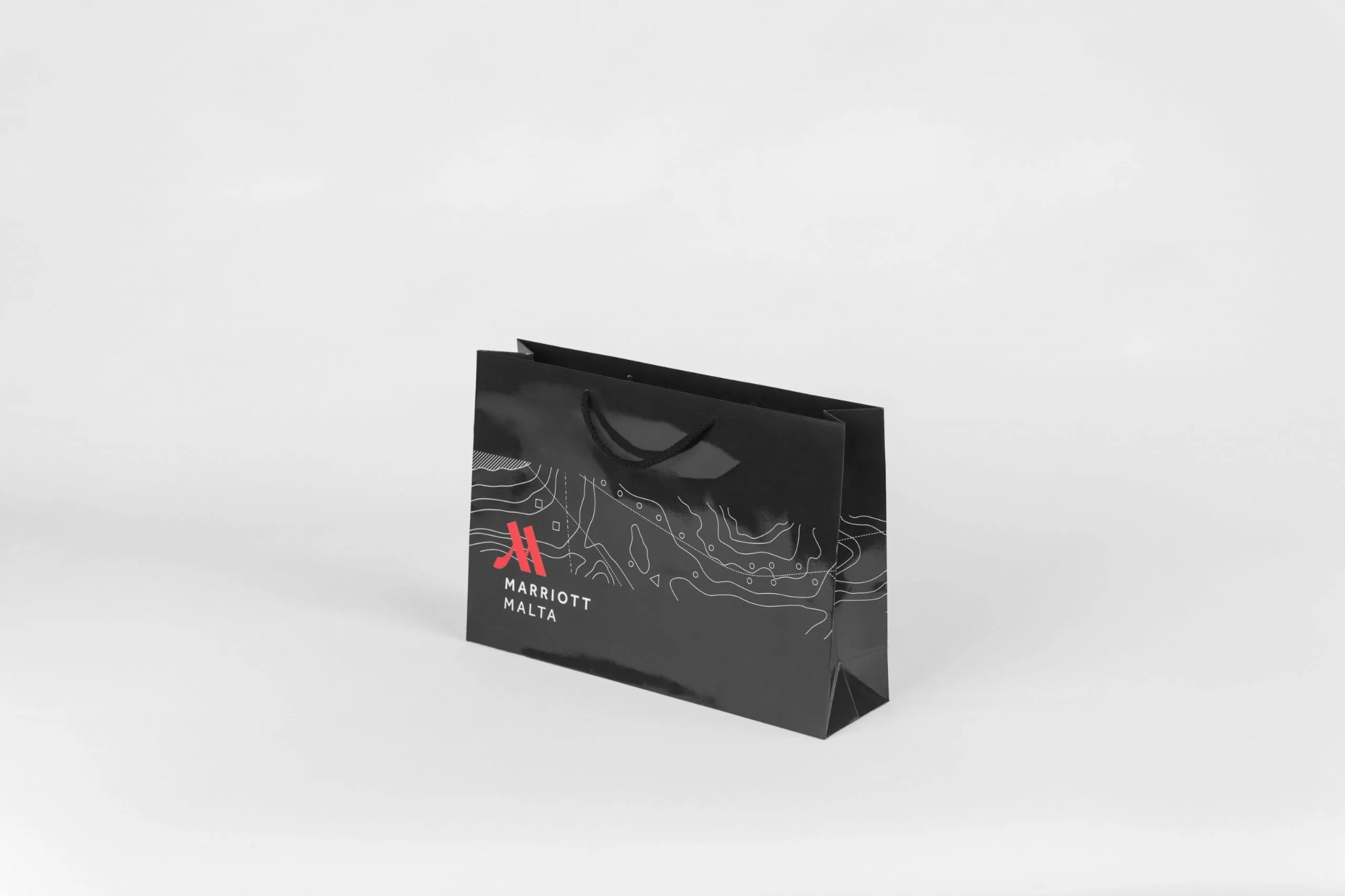 Czarna, lakierowana torba prezentowa z nadrukiem logo Marriott Malta i graficznym motywem mapy na białym tle.