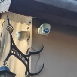 Dwie kamery monitoringu Tiandy zamontowane na elewacji budynku, widoczne przewody oraz ozdobny, metalowy element dekoracyjny.