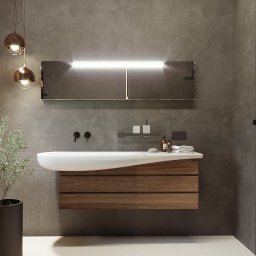 Inargo - Nowoczesna łazienka z wiszącą szafką z drewnianymi frontami, umywalką o organicznym kształcie i podświetlanym lustrem na tle szarej ściany z betonową fakturą, uzupełniona dekoracyjną rośliną...