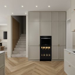 Inargo - Beżowa kuchnia na wymiar w Trzebnicy, z zabudowaną chłodziarką na wino i piekarnikiem, widok na salon i schody.
