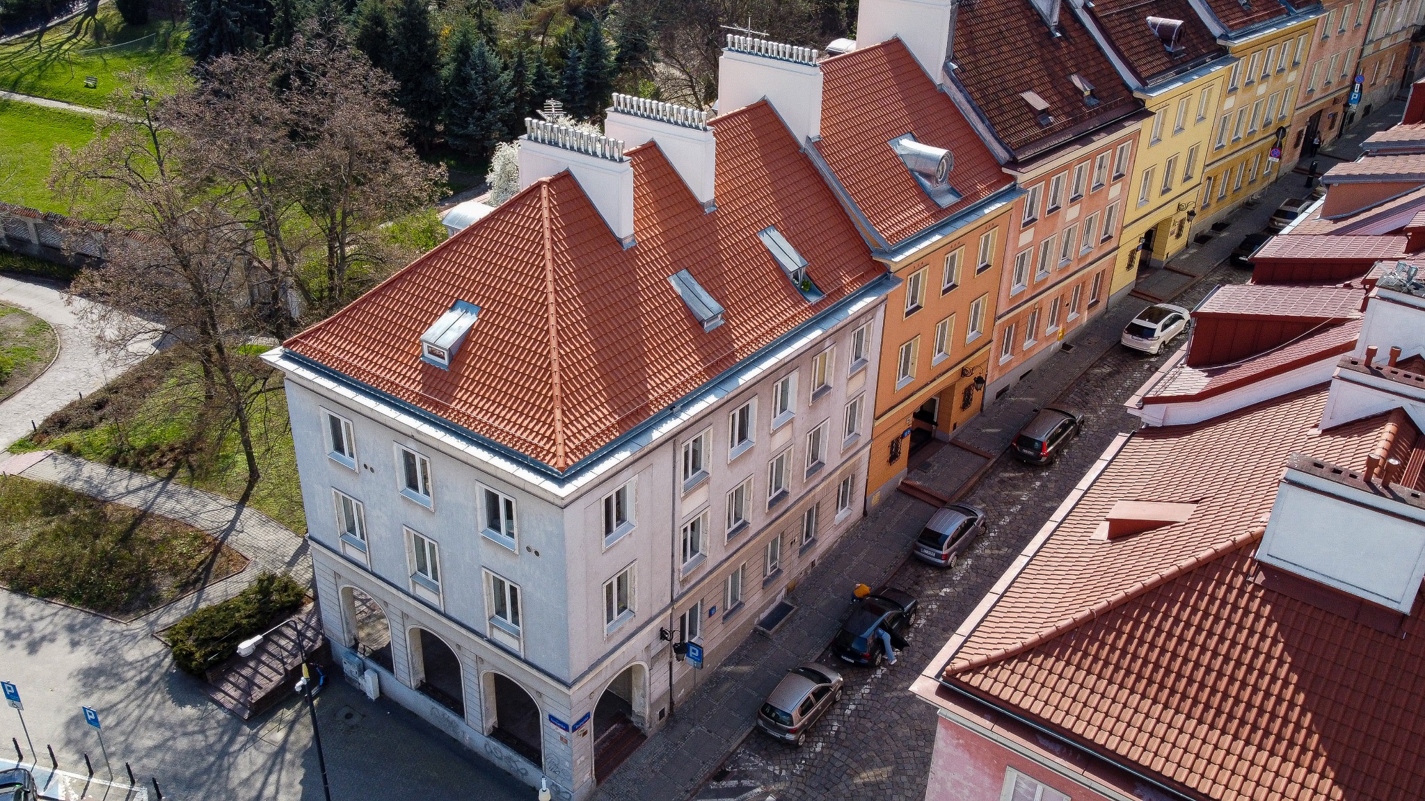 Widok z góry na odnowione dachy z czerwonej dachówki w kamienicach na Starym Mieście, widoczne okna dachowe i detale architektoniczne.