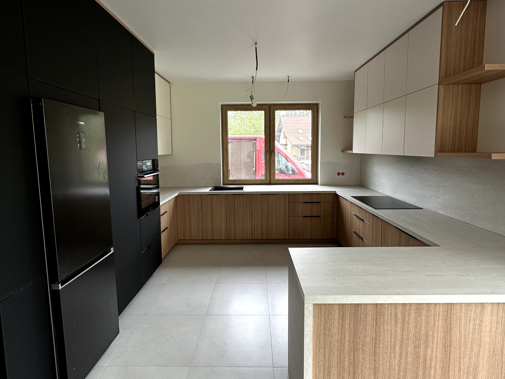 Nowoczesna kuchnia w trakcie montażu: czarne szafki, drewnopodobne fronty dolne, jasnoszare blaty, widoczne niedokończone podłączenia oświetlenia sufitowego.