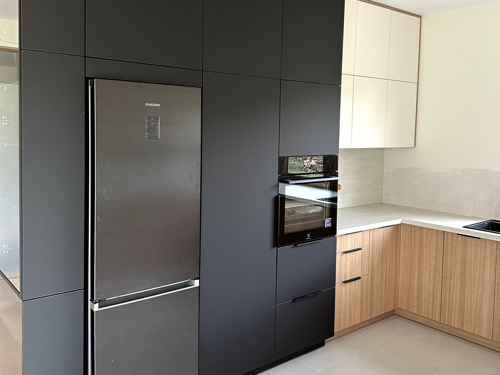 Nowoczesna kuchnia: zabudowa w kolorze grafitowym z lodówką Samsung i piekarnikiem Electrolux, jasne drewniane szafki dolne i białe górne, szary blat.