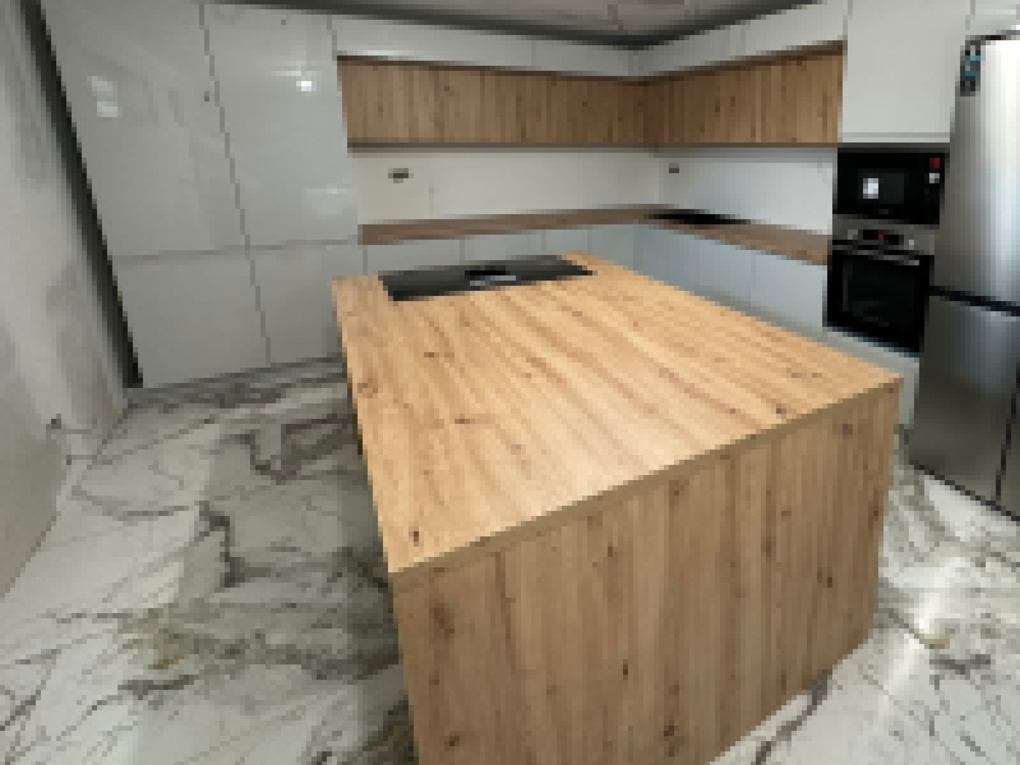 Nowoczesna kuchnia z wyspą o drewnianym blacie, jasne fronty szafek i marmurowa podłoga.