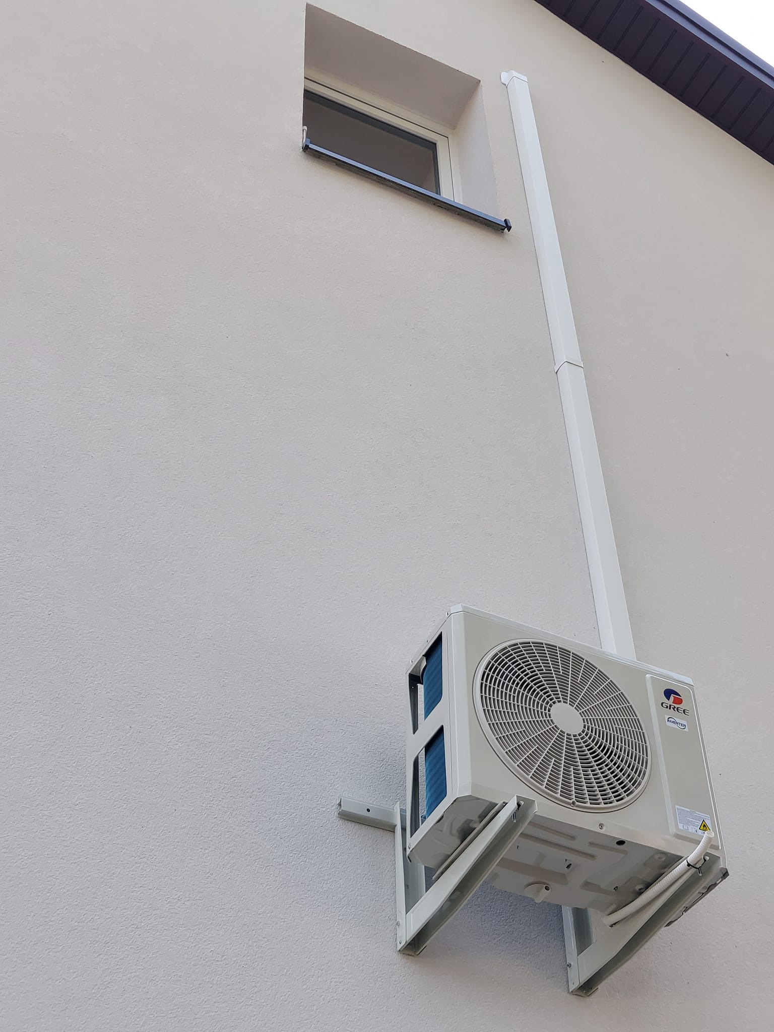 Klimatyzator marki Gree zamontowany na elewacji domu w pobliżu okna i rury spustowej.