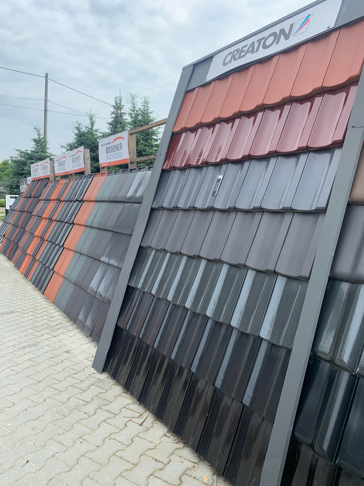 Ekspozycja dachówek Creaton i Bogener Dachziegel w różnych kolorach i odcieniach, ułożonych na stojaku prezentacyjnym na zewnątrz.