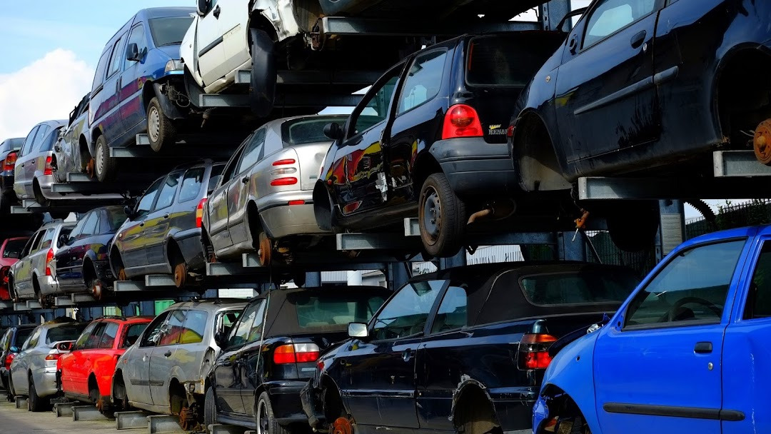 Wrakowisko samochodowe: wielopoziomowy parking z uszkodzonymi pojazdami, widoczne braki kół, różne kolory karoserii, ujęcie z dołu pod kątem.