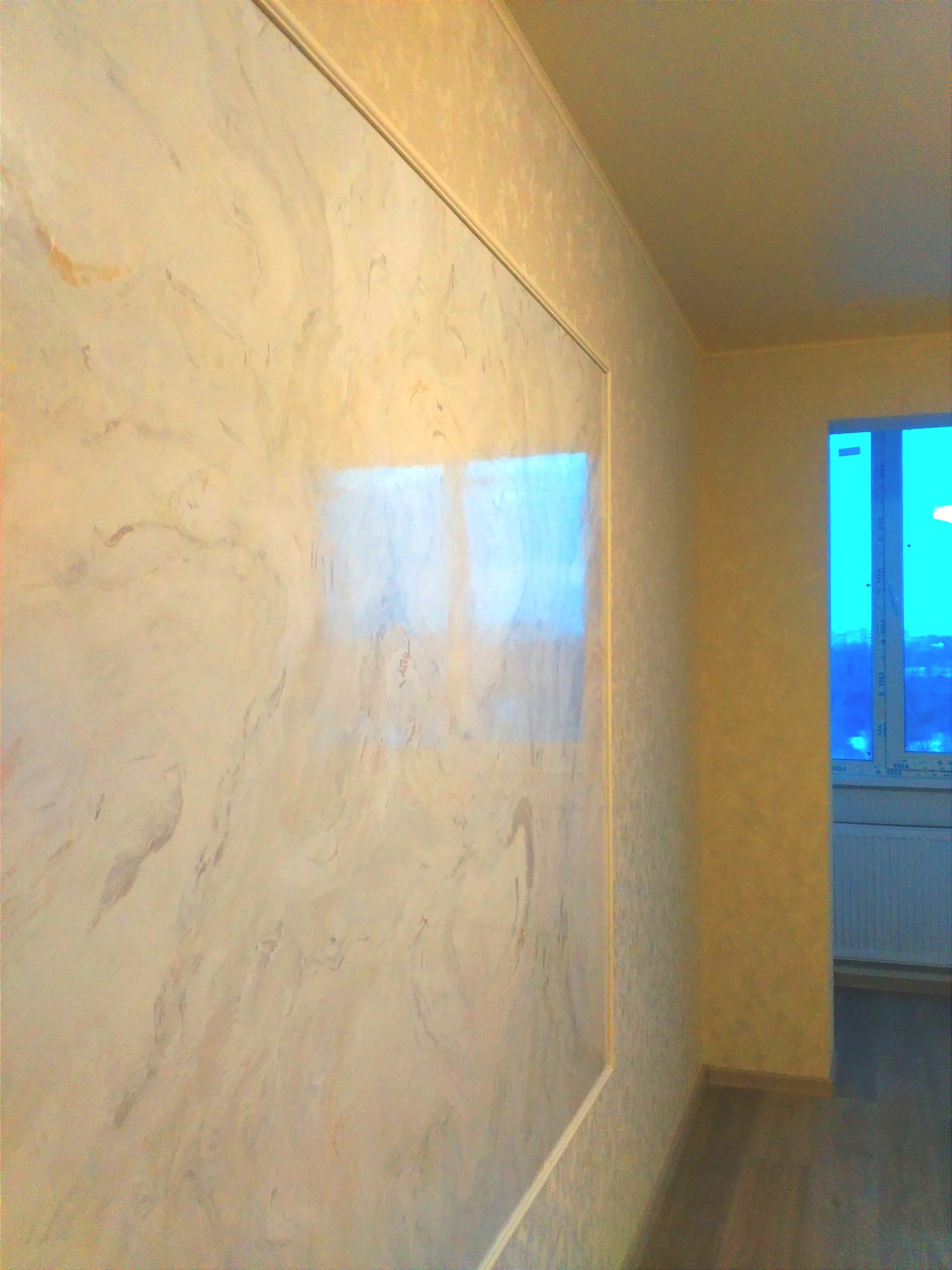 Ściana z dekoracyjną fakturą w odcieniach beżu i brązu, obramowana listwą, widok z perspektywy, okno w tle.