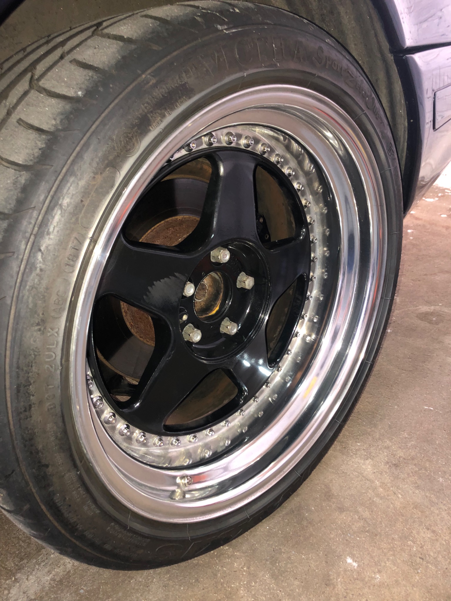 Błyszczące, czarne felgi aluminiowe z chromowanym rantem i oponą Victoria Sport Z na tle betonowej podłogi garażu.