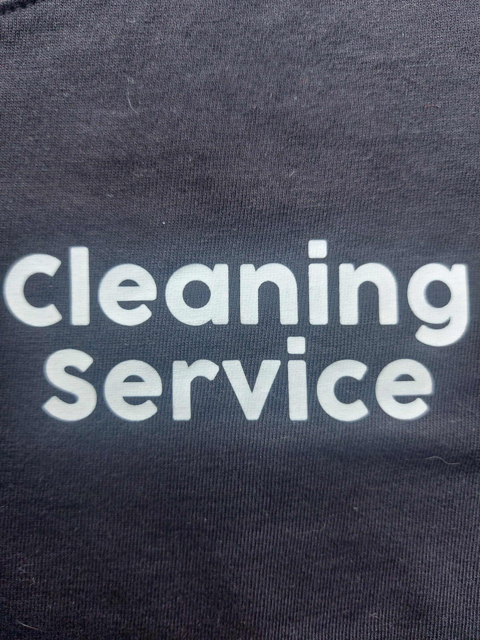 Ciemna koszulka z nadrukiem 'cleaning service' w kolorze białym, widoczna faktura materiału.