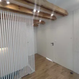 Nowoczesne wnętrze z drewnianym sufitem, białymi lamelami jako ścianką działową i dekoracyjnymi panelami ściennymi, ukryte drzwi.