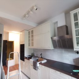 Jakość Zrobimy - Jasna kuchnia w trakcie odświeżania, widoczna drabina, umywalka z naczyniami i akcesoriami malarskimi, oraz oświetlenie sufitowe.