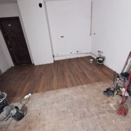 Jakość Zrobimy - Fragment pokoju z częściowo ułożonymi panelami podłogowymi imitującymi drewno, widoczne stare panele, narzędzia i akcesoria glazurnicze.