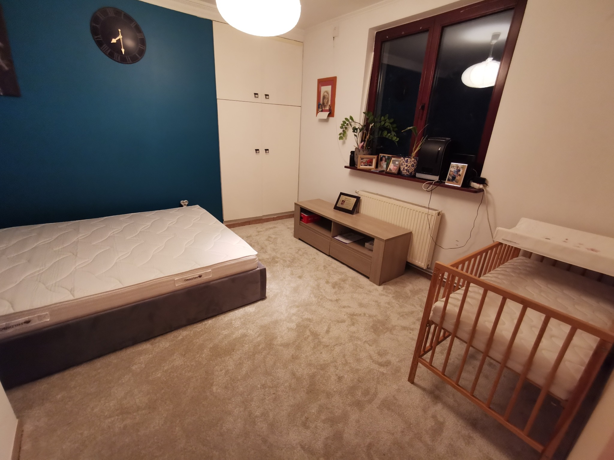 Pokój dziecięcy z łóżeczkiem, łóżkiem z materacem Hilding, szafą w zabudowie, ścianą pomalowaną na niebiesko i dywanem w odcieniach beżu.