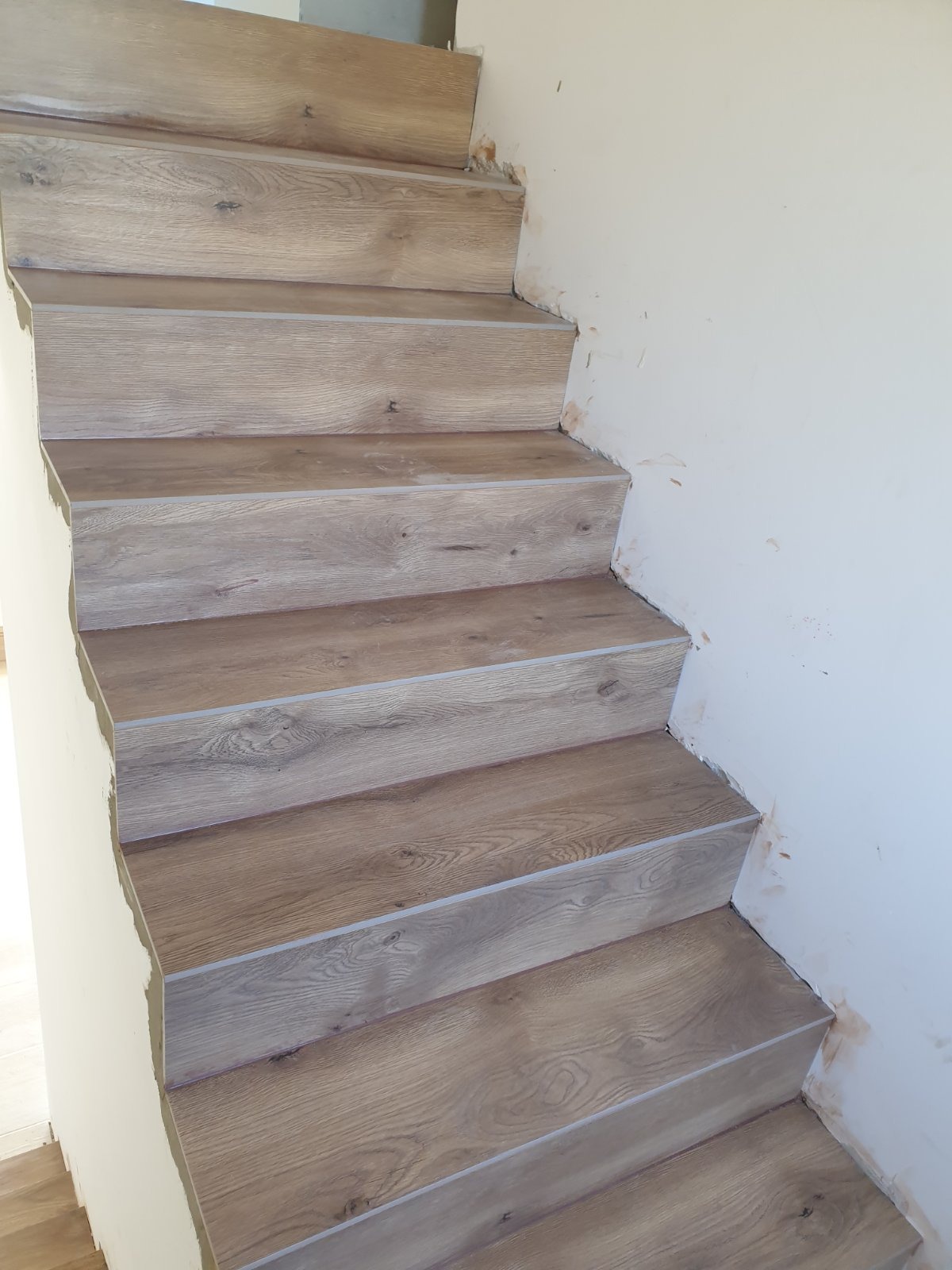 Schody wyłożone panelami imitującymi drewno, widoczne ślady zaprawy na ścianie po montażu.