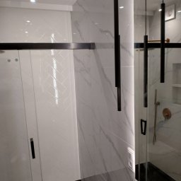 Dawid Mazelewski - Nowoczesna łazienka z kabiną prysznicową, białymi płytkami ułożonymi w jodełkę, marmurowymi panelami ściennymi i minimalistycznymi lampami wiszącymi.