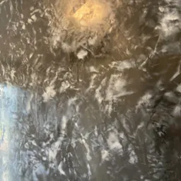 Ściana z efektem dekoracyjnym w odcieniach szarości i bieli, imitująca marmur, z widocznym refleksem światła u góry.