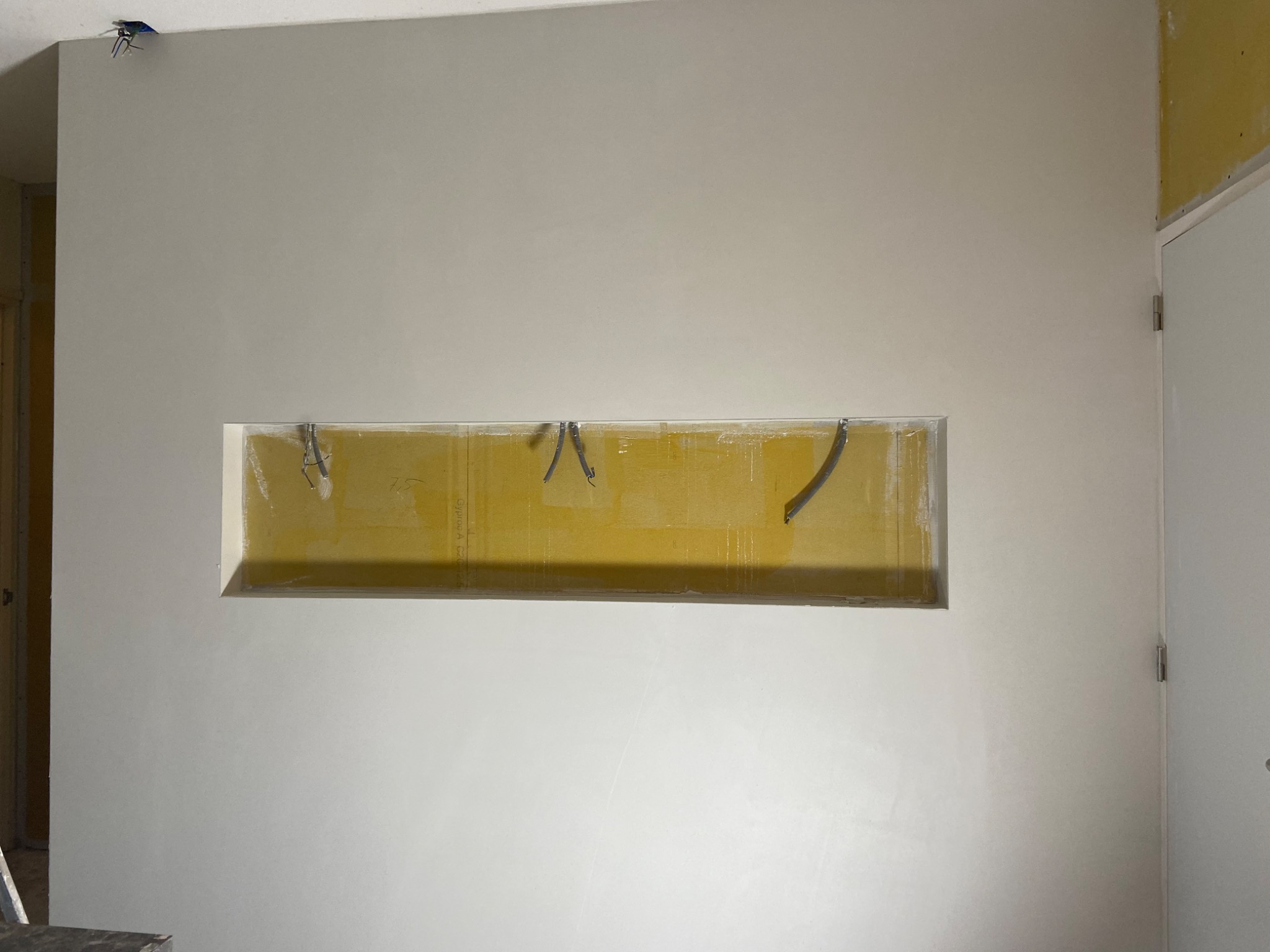 Ściana po nałożeniu gładzi, z widoczną wnęką przygotowaną do dalszego wykończenia, wystające przewody elektryczne u góry ściany.