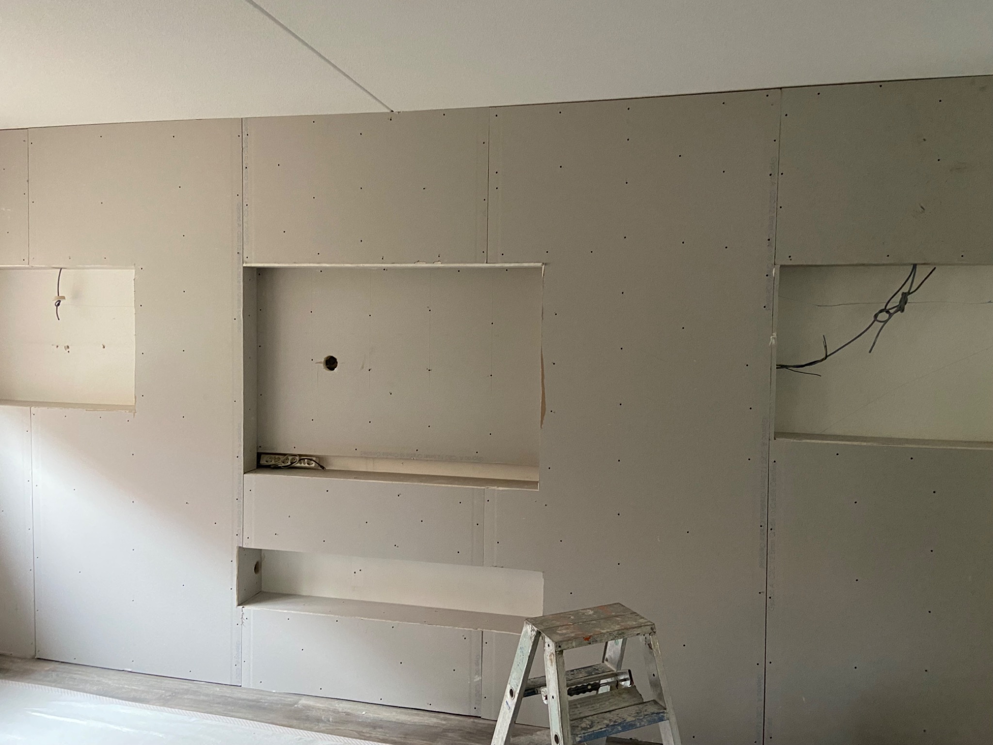 Ściana z płyt gipsowo-kartonowych z wnękami, widoczna drabina malarska, surowy stan przed wykończeniem
