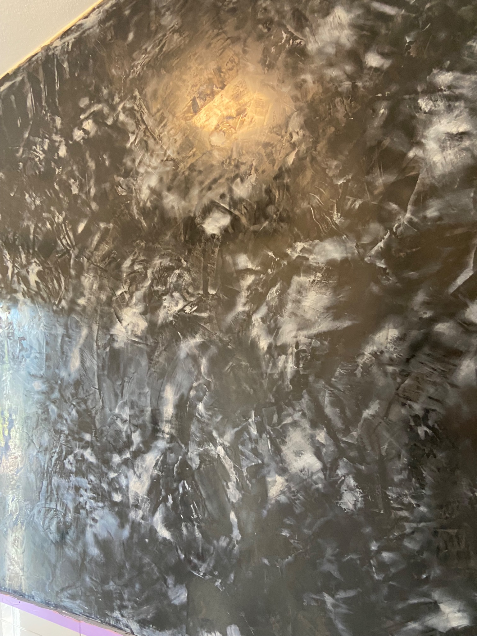 Ściana z efektem dekoracyjnym w odcieniach szarości i bieli, imitująca marmur, z widocznym refleksem światła u góry.