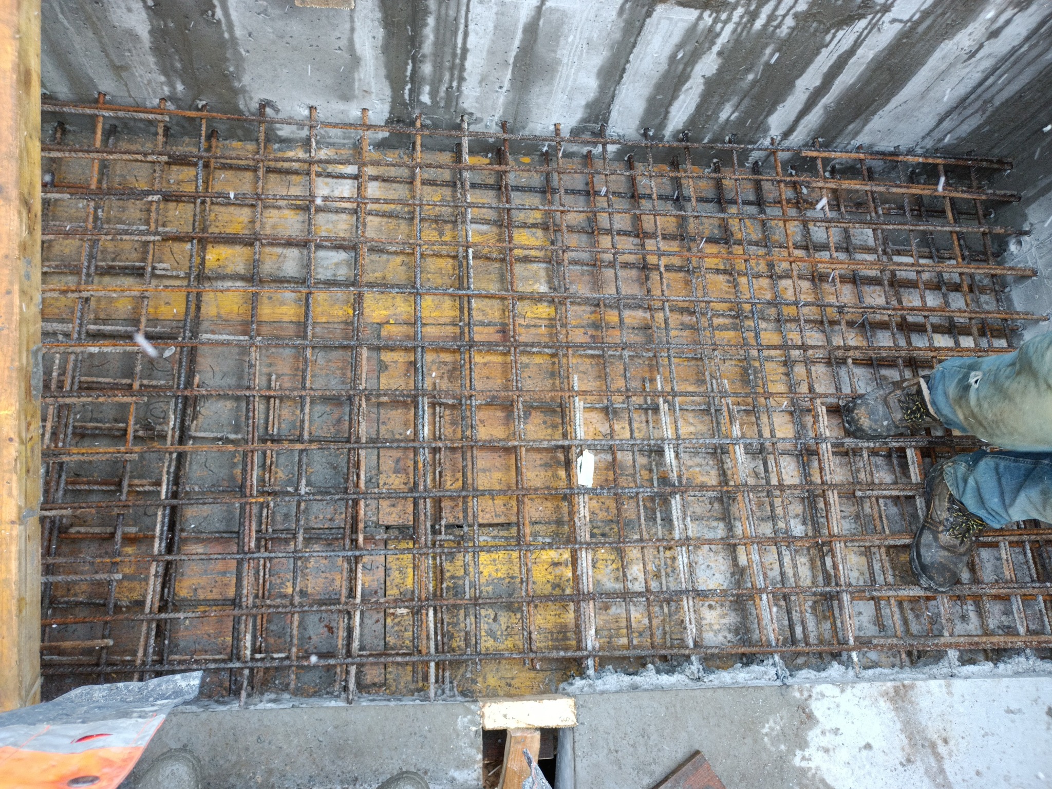 Zbrojenie fundamentów z widocznymi elementami szalunku i fragmentem roboczych butów w Świętochłowicach.