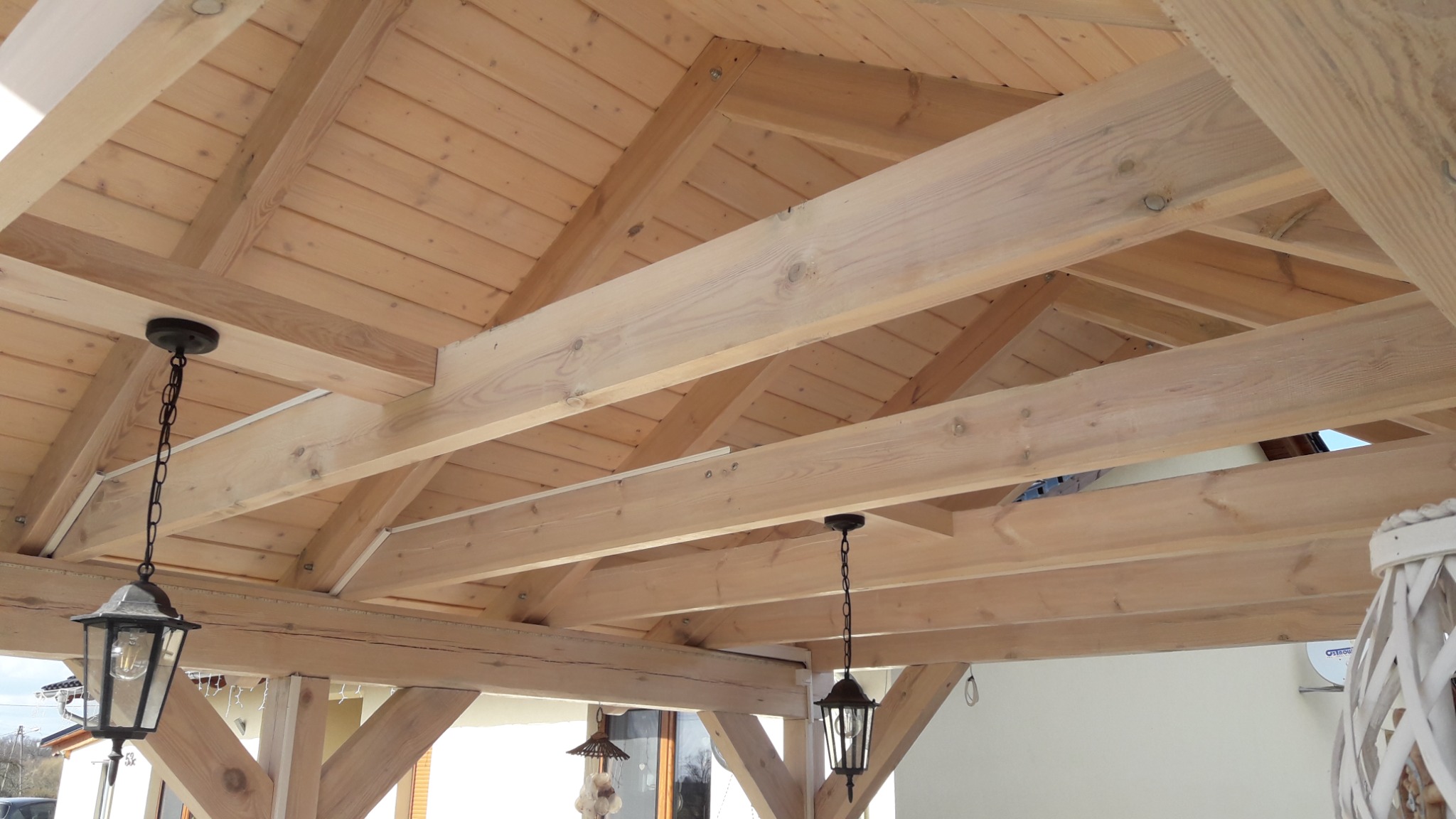 Drewniana konstrukcja z belek i desek, widoczne elementy oświetlenia w stylu retro, jasne drewno.