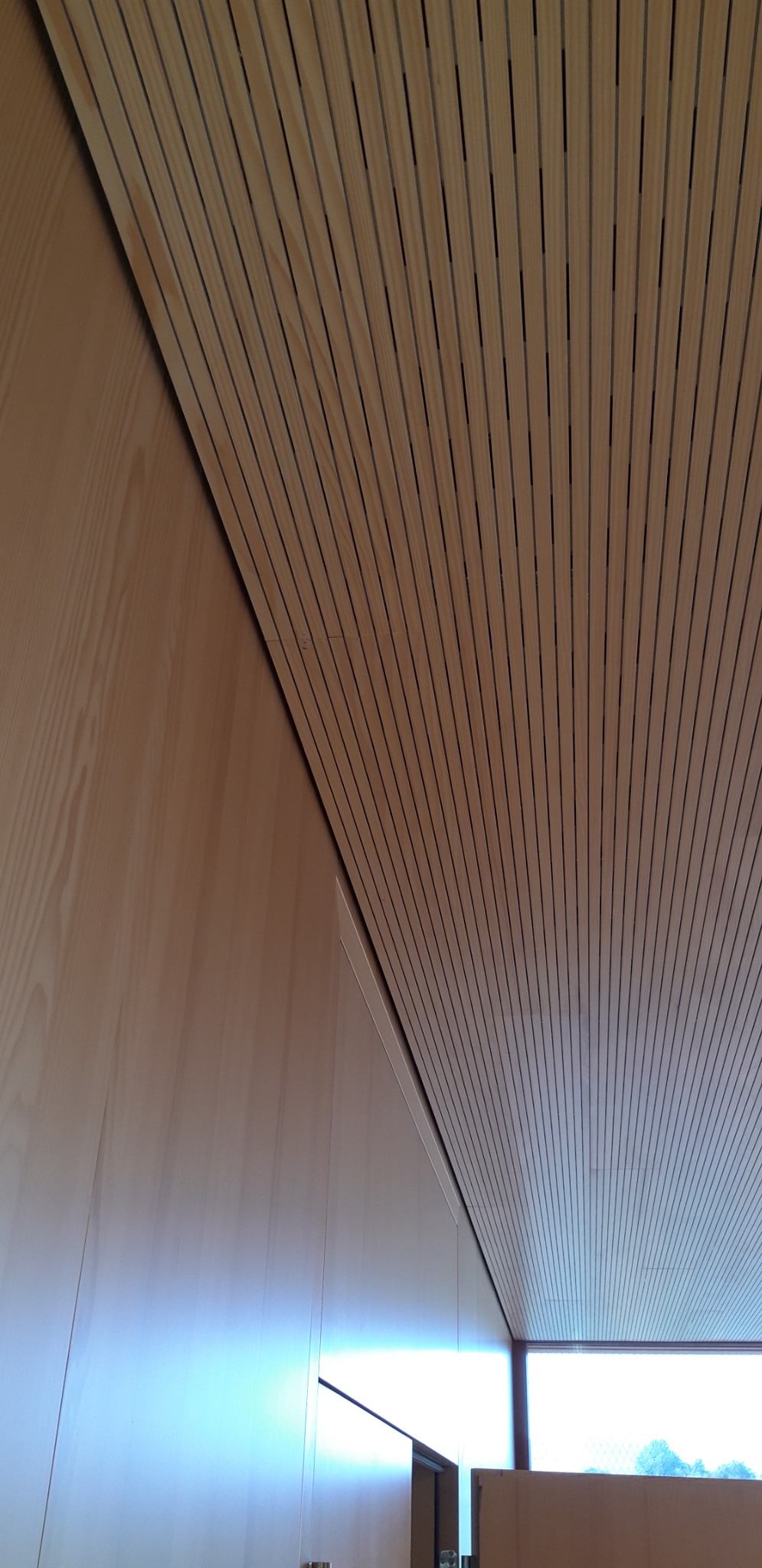 Drewniany sufit lamelowy z widocznymi szczelinami, połączony z drewnianą ścianą, z oknem w tle.