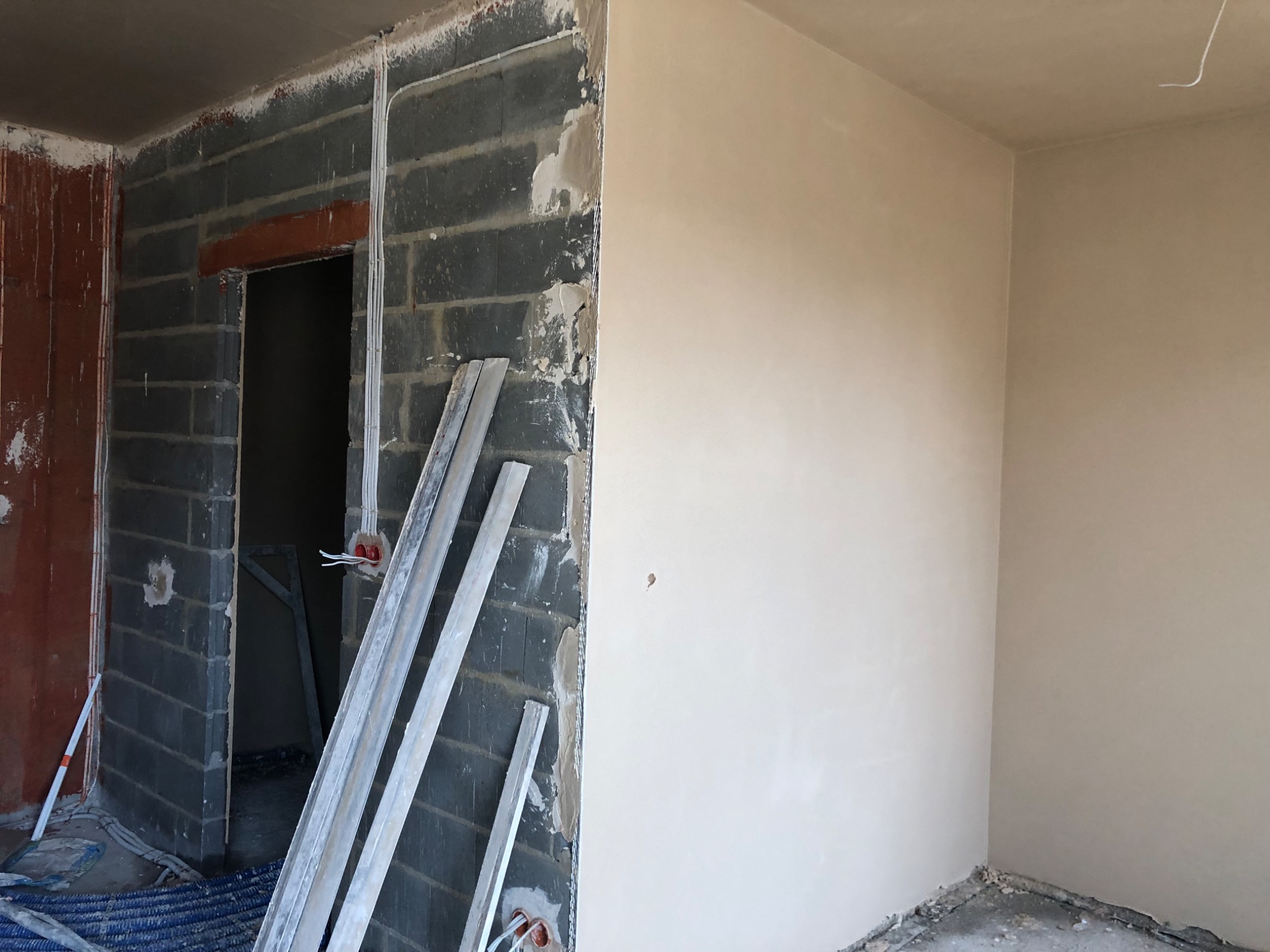 Ściana z nałożonym tynkiem maszynowym w trakcie prac wykończeniowych, widoczne bloczki betonowe, instalacja elektryczna i listwy tynkarskie.