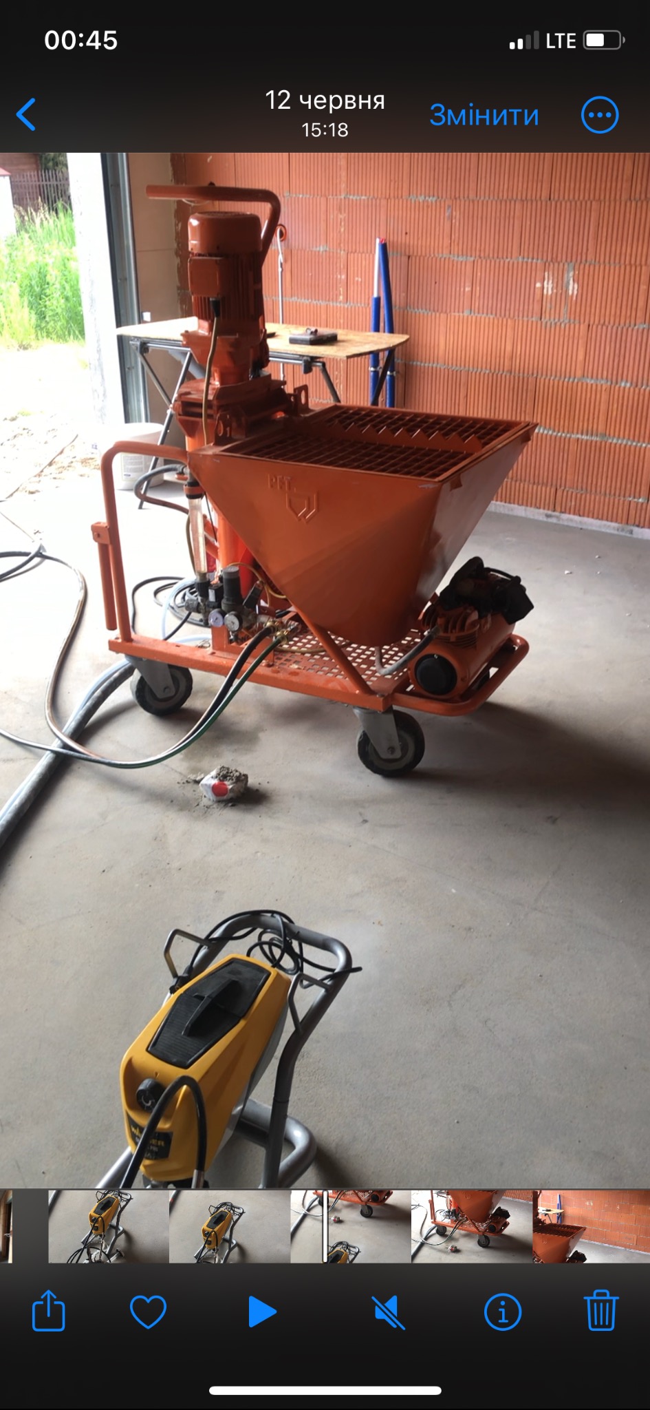 Pomarańczowa maszyna do tynkowania z żółtym agregatem natryskowym na betonowej podłodze w surowym wnętrzu z ceglaną ścianą w tle.