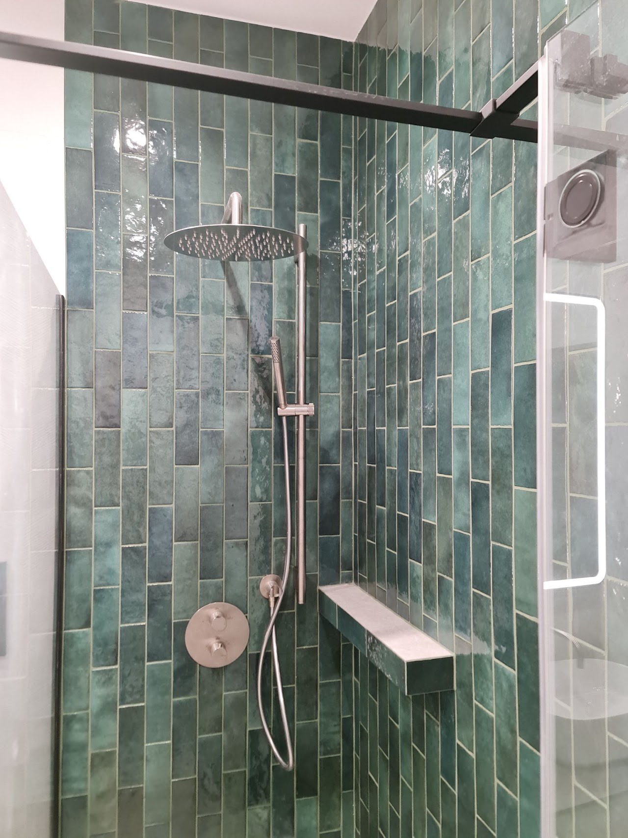 Kabina prysznicowa z zielonymi, błyszczącymi płytkami ułożonymi pionowo, srebrna armatura i półka w kabinie, Alwernia.