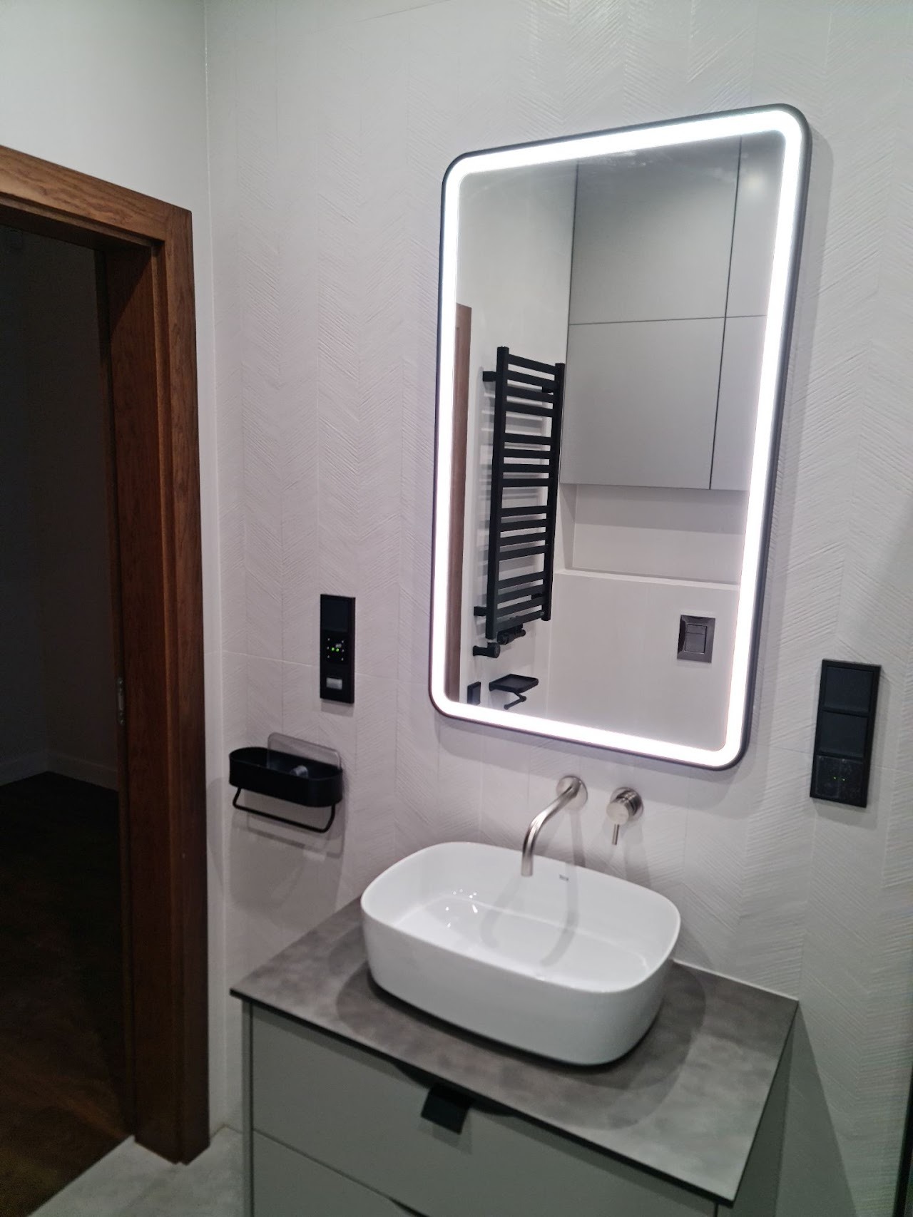 Umywalka nablatowa w nowoczesnej łazience z podświetlanym lustrem i grzejnikiem drabinkowym widocznym w odbiciu.