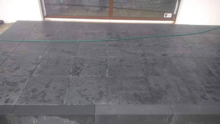 Nowo ułożona, ciemnoszara kostka granitowa na tarasie przy oknie, widoczny zielony wąż ogrodowy.