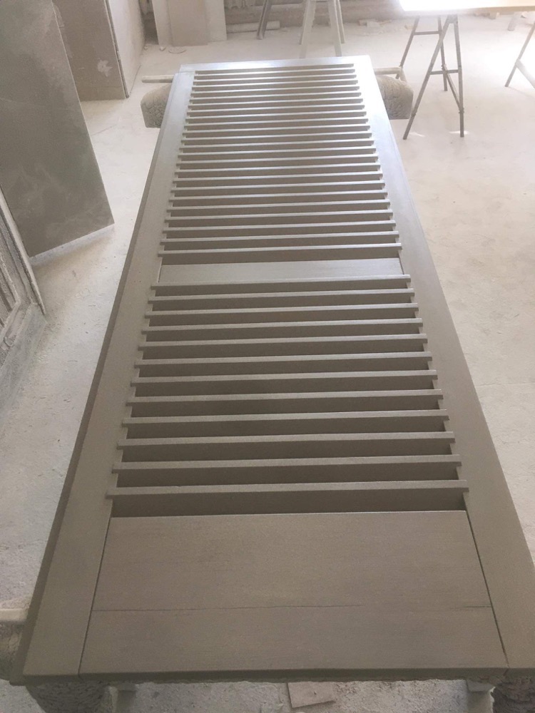 Szara, drewniana, surowa, niedokończona wewnętrzna okiennica z lamelami leżąca na stole w warsztacie.