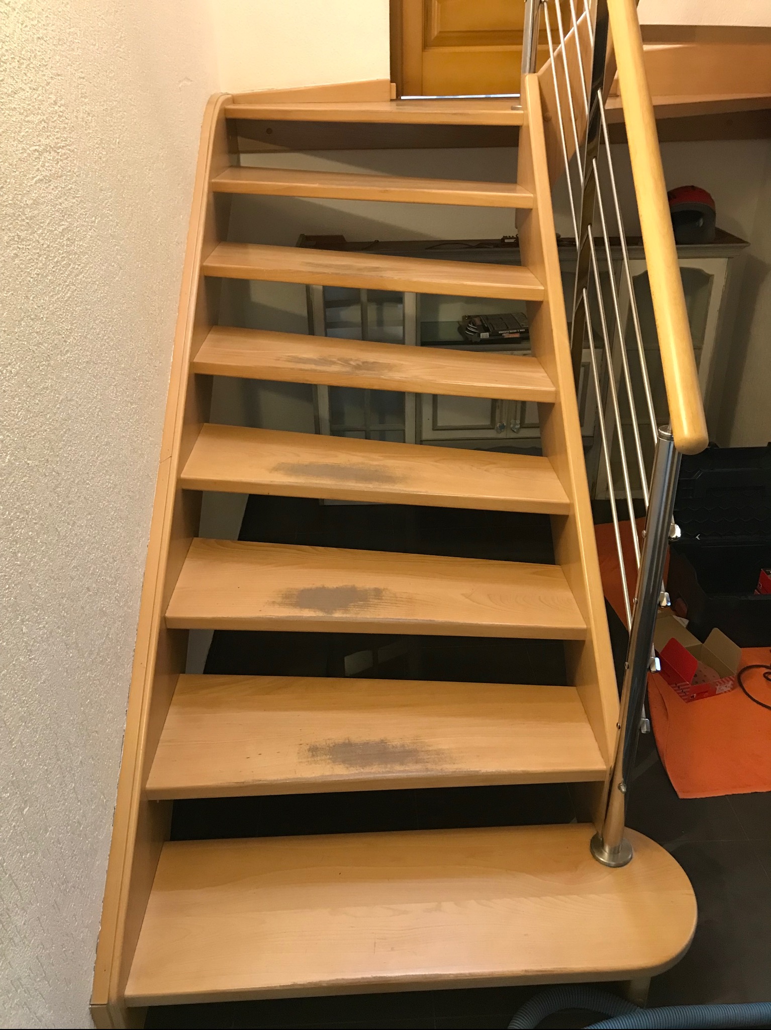 Drewniane schody z metalową balustradą, widoczne ślady użytkowania na stopniach, tło z teksturą ściany i elementami wyposażenia wnętrza.