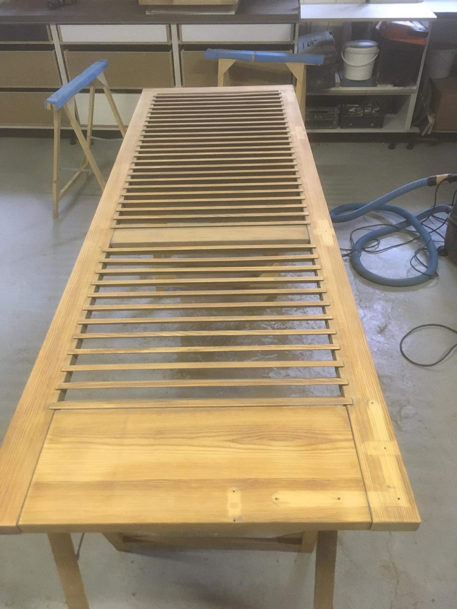 Drewniane drzwi lamelowe w trakcie renowacji, leżące na stole w warsztacie, widoczne ślady obróbki drewna i akcesoria warsztatowe.