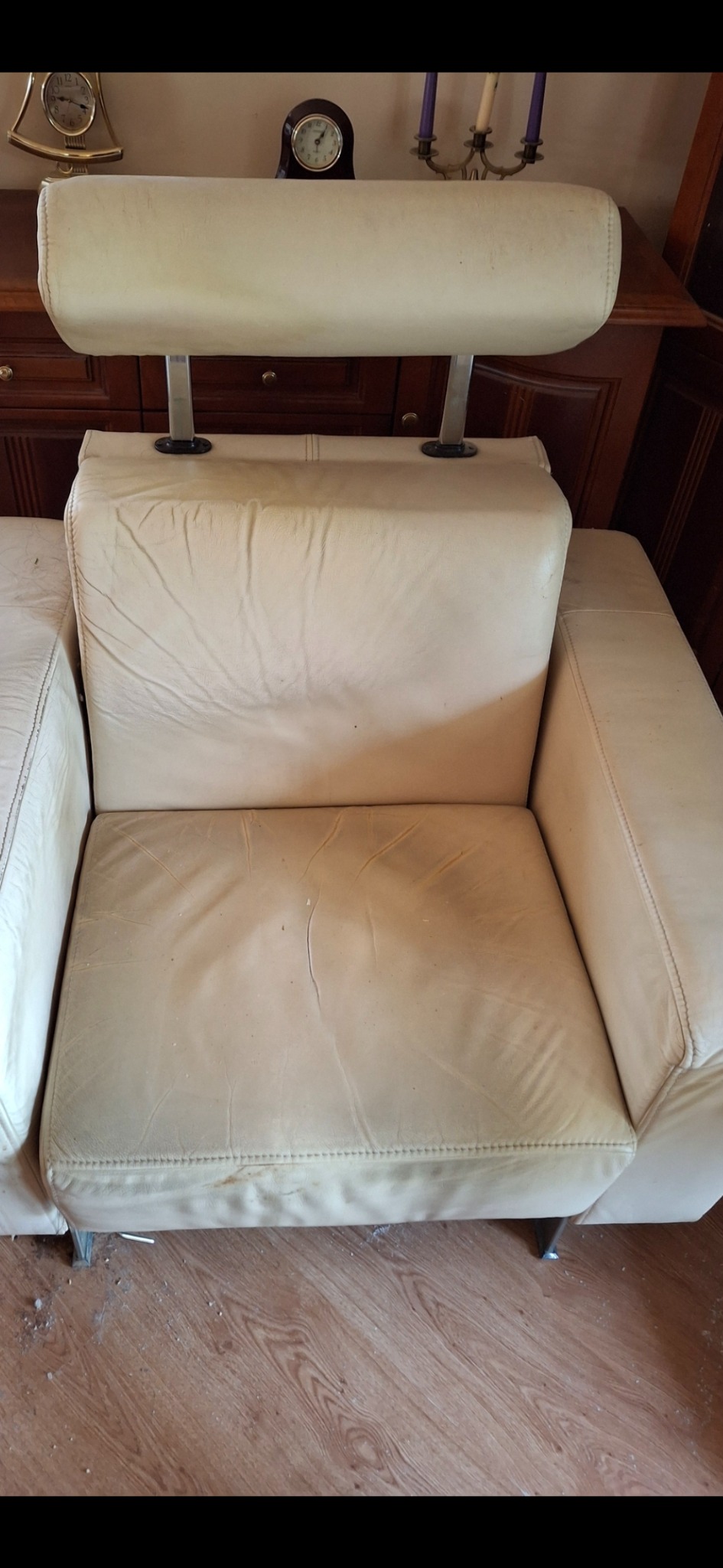 Beżowy, skórzany fotel z regulowanym zagłówkiem na tle drewnianych mebli i podłogi. Widoczne ślady użytkowania na siedzisku i podłodze.