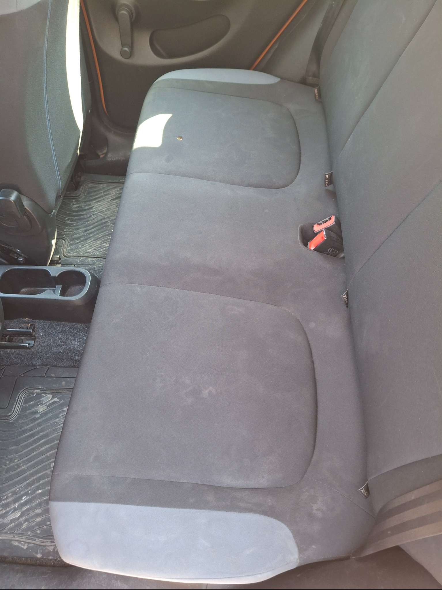 Brudna, szara tapicerka tylnej kanapy w samochodzie Smart z widocznymi plamami i zabrudzeniami na siedzeniu oraz dywanikach. Widoczne mocowania ISOFIX.
