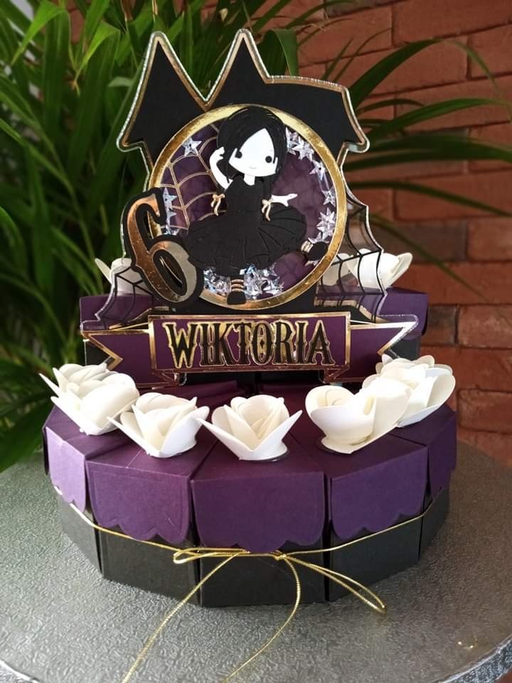 Ozdobny tort z topperem inspirowanym Wednesday Addams, z imieniem Wiktoria, dekorowany papierowymi różami i złotą wstążką na srebrnej tacy.